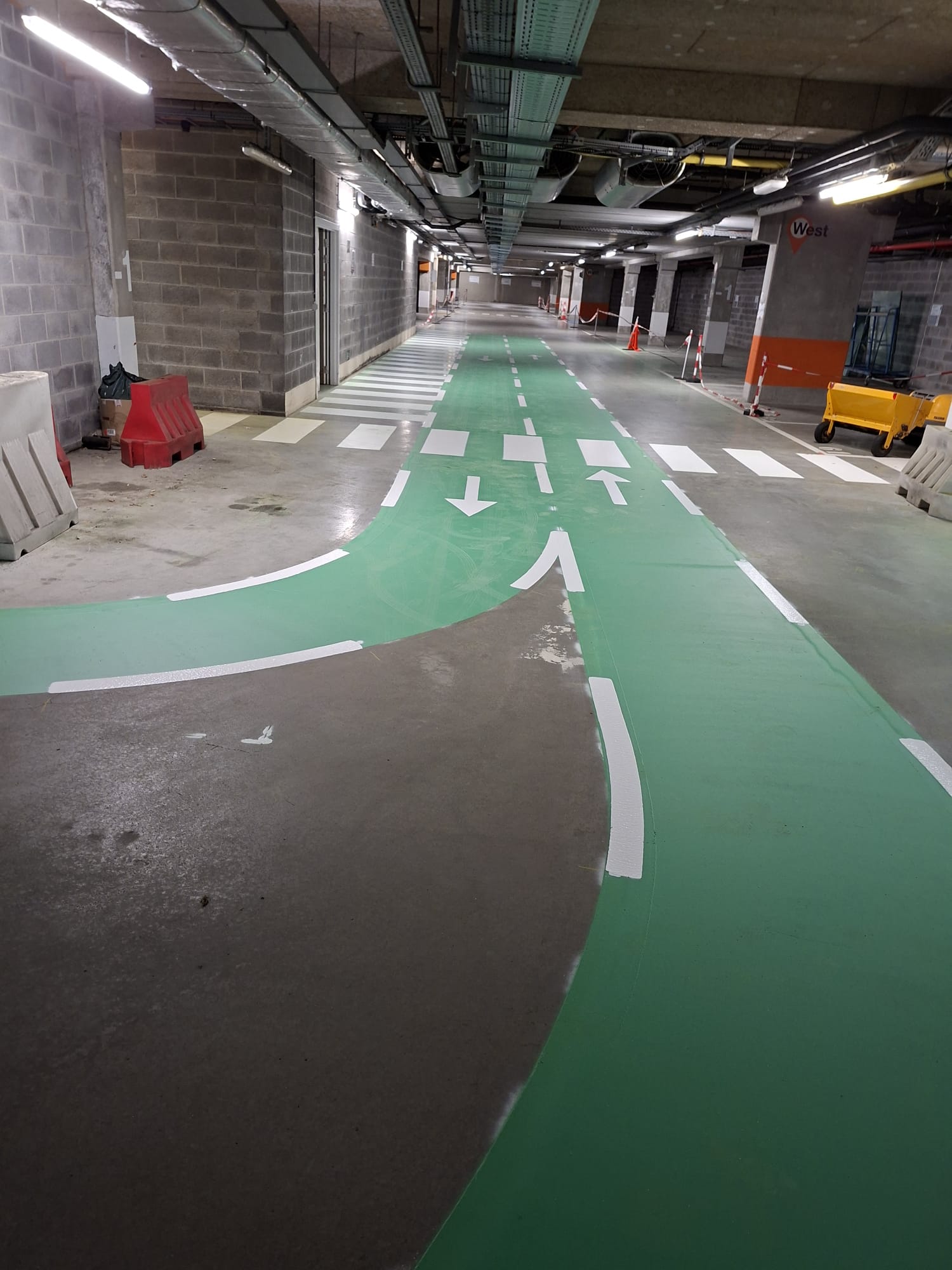 Ondergrondse parking met groen-gekleurd fietspad, witte pijlen en zebrapad